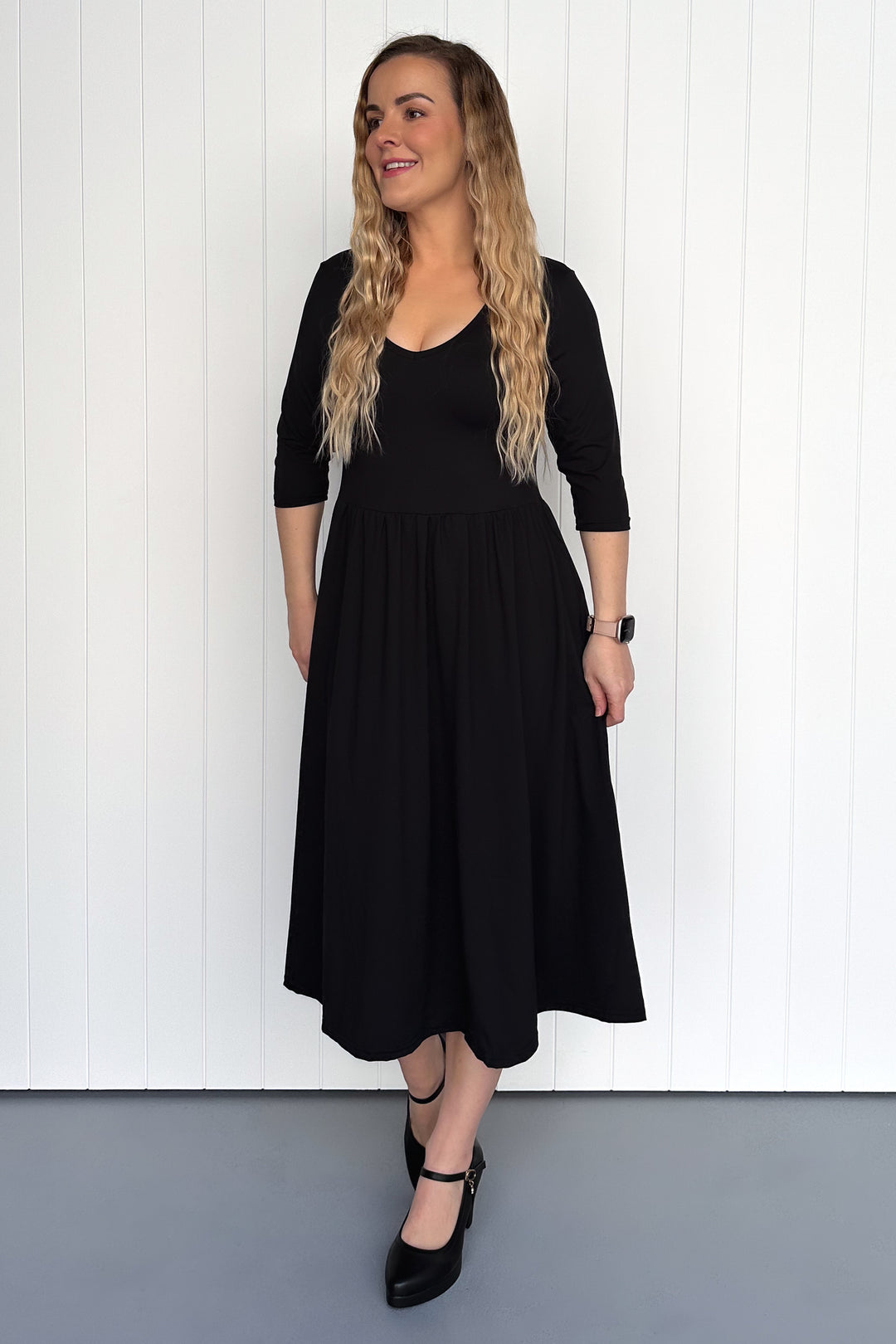 Woman wearing a black dress against a white wooden panel background