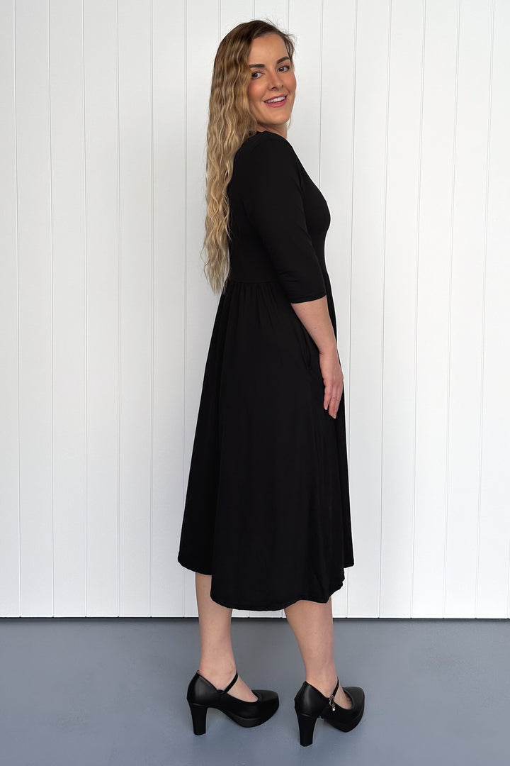 Woman wearing a black dress standing against a white paneled wall.
