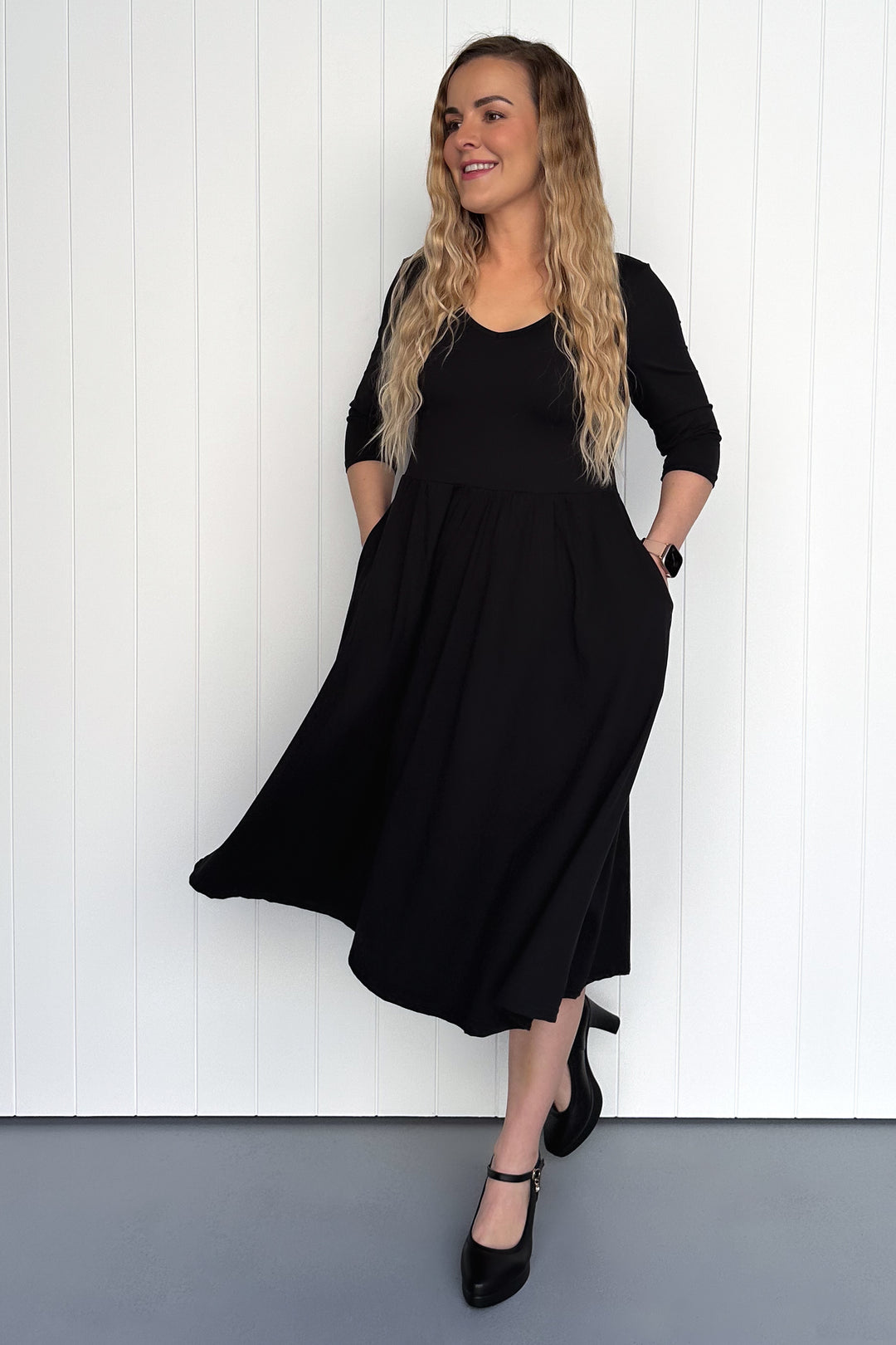 Woman wearing a black dress standing against a white wall.