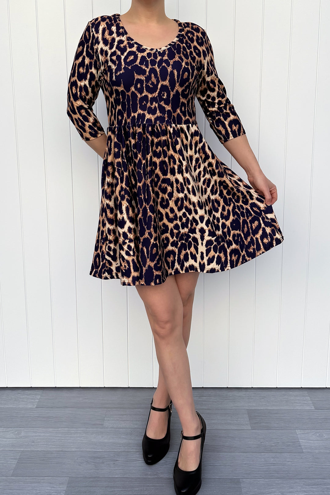 Person wearing a leopard print dress against a white wooden panel background