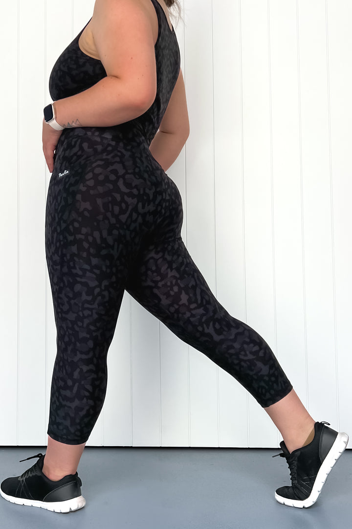 Person wearing a black leopard print outfit with sneakers against a white wall.