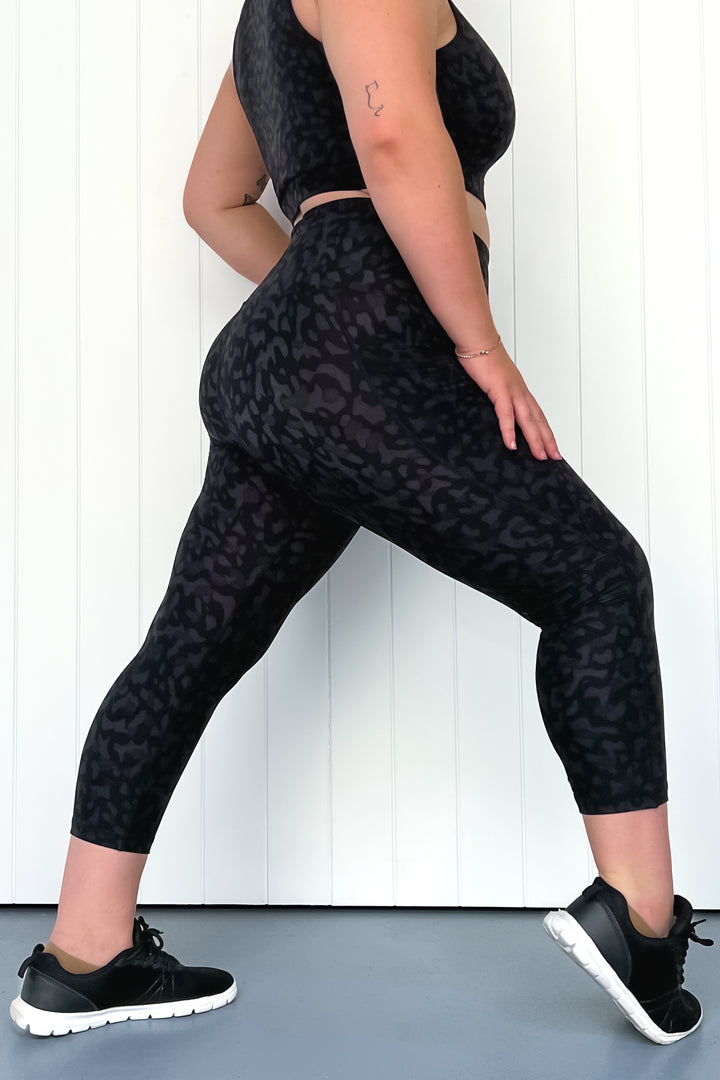 Person wearing black leopard print leggings and black sneakers on a white background