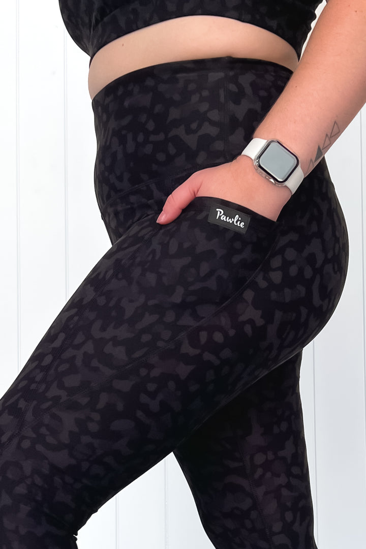 Person wearing black leopard print leggings with a visible brand logo on a white background
