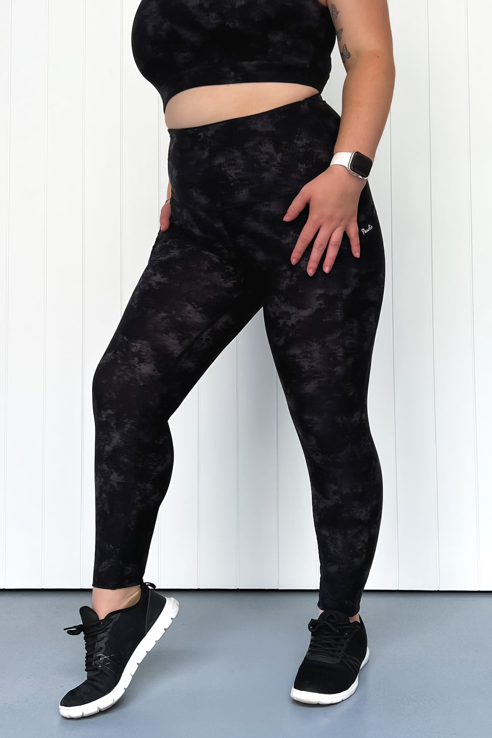 Person wearing black tie-dye leggings and black sneakers on a white background