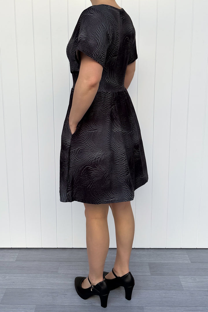 Person wearing a black leather patterned dress against a white wooden panel background
