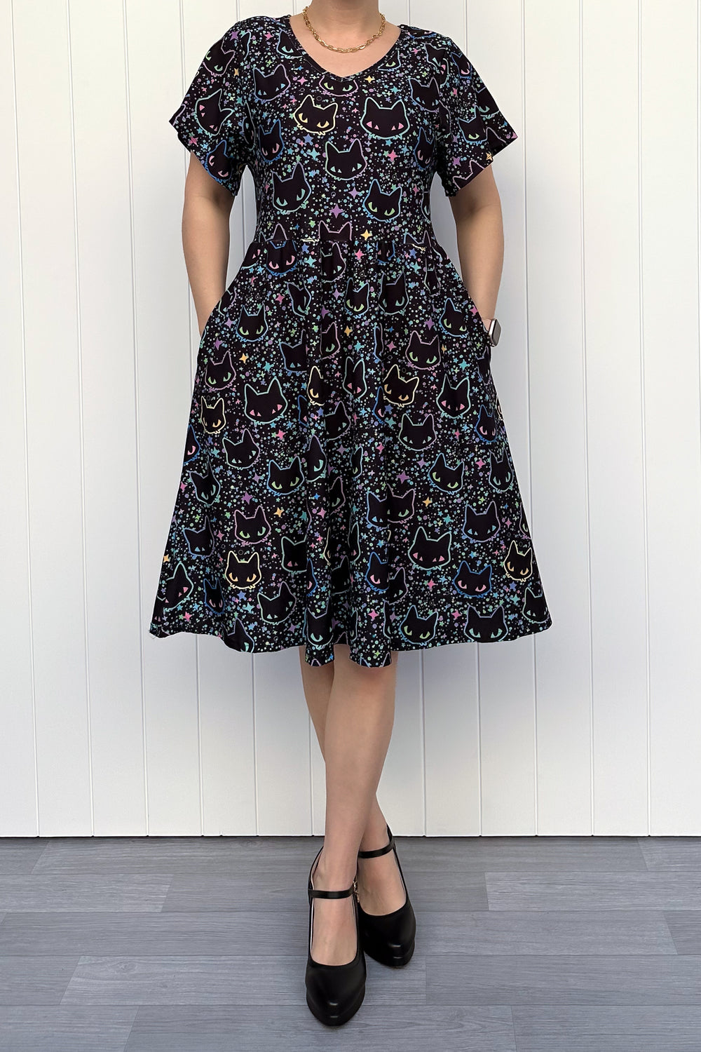 Person wearing a black dress with cat pattern against a white wooden panel background