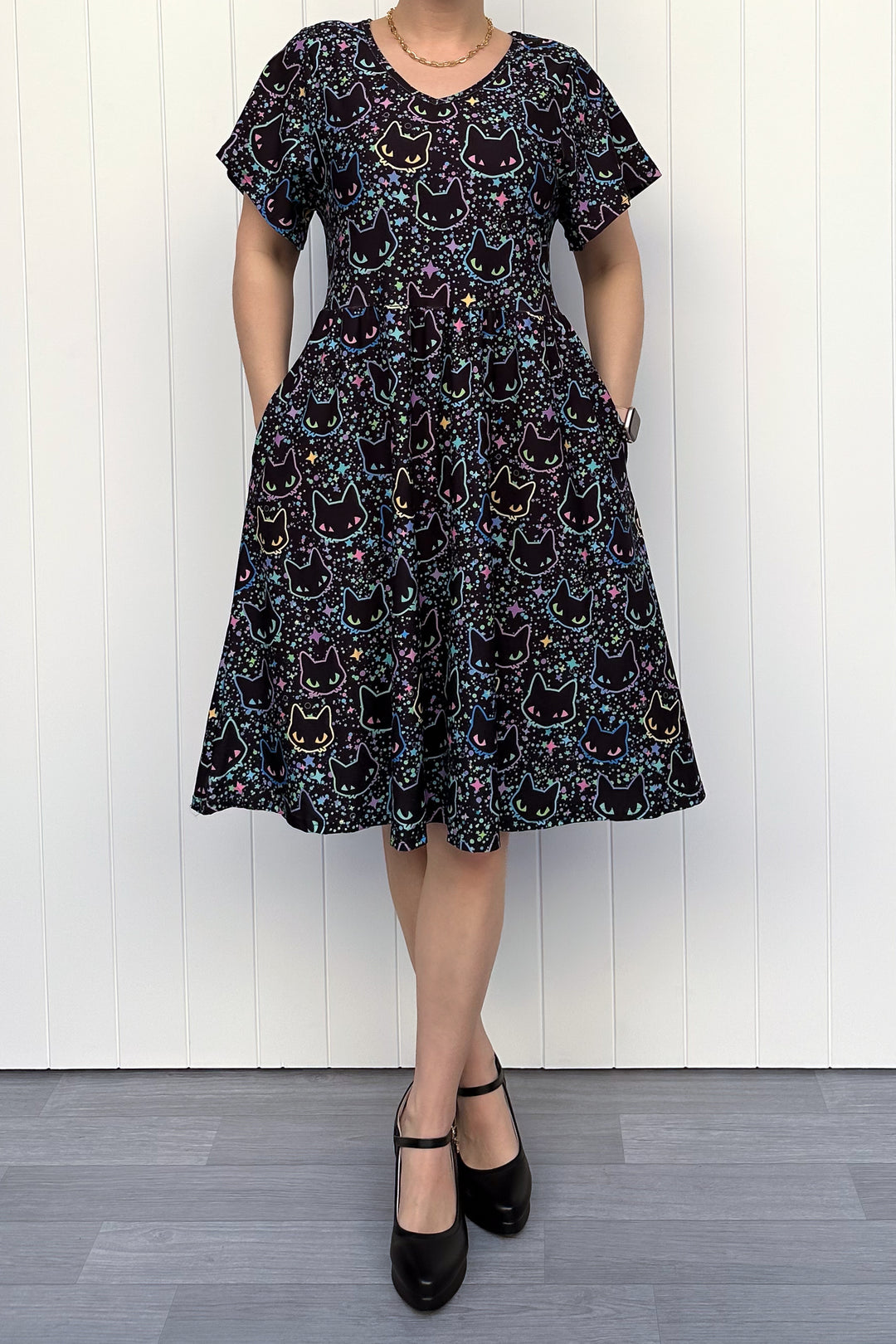 Person wearing a black dress with cat pattern against a white wooden panel background
