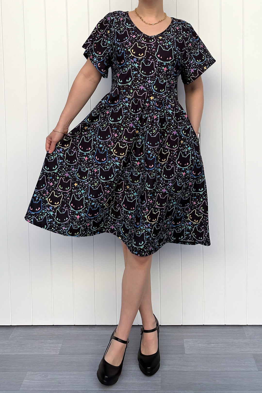Person wearing a black dress with cat pattern against a white wooden panel background
