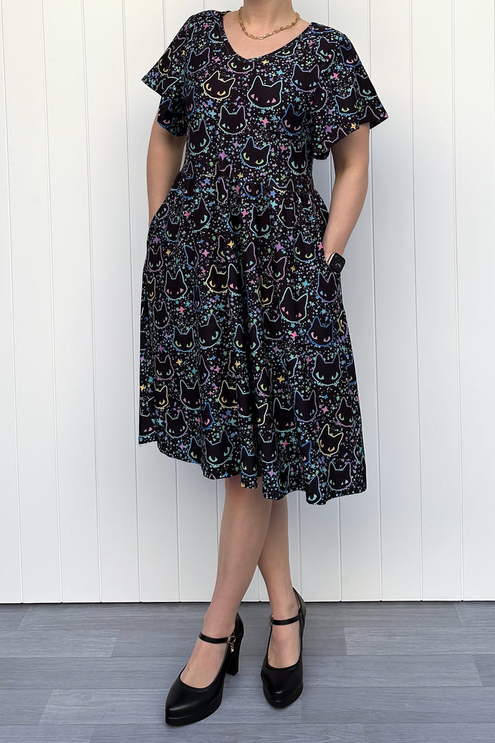Person wearing a black dress with colorful cat pattern against a white wooden panel background