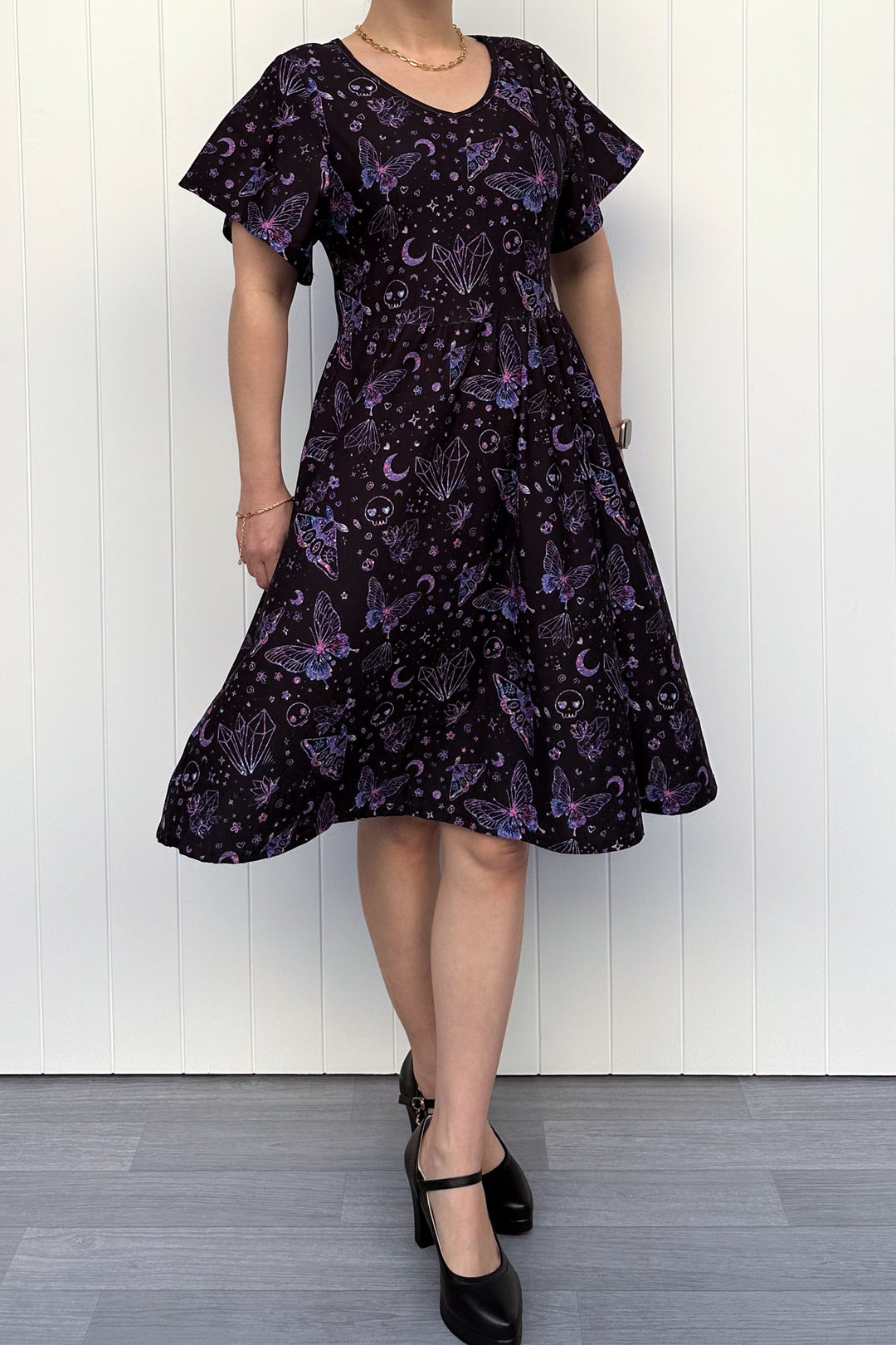 Person wearing a glitter purple dress with witch, skull and butterfly pattern against a white wooden panel background