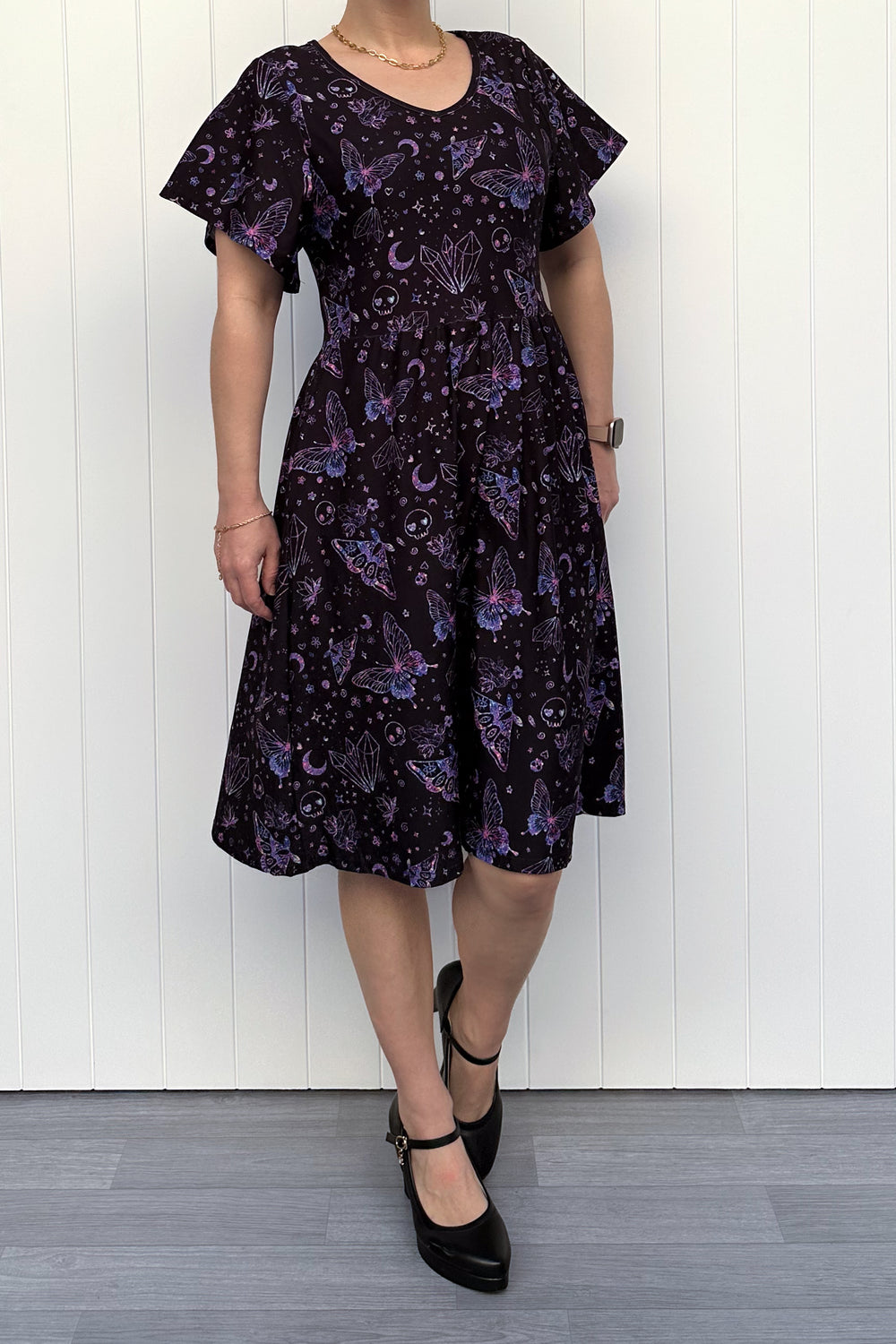 Person wearing a glitter purple dress with witch, skull and butterfly pattern against a white wooden panel background