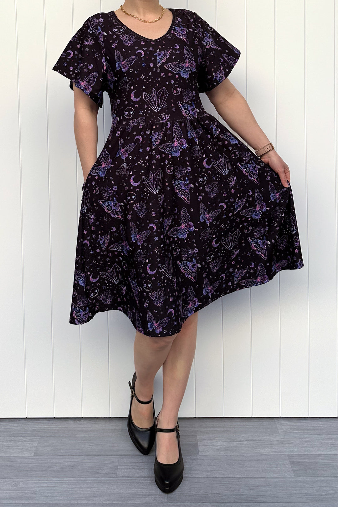 Person wearing a dark purple dress with celestial pattern against a white wooden panel background