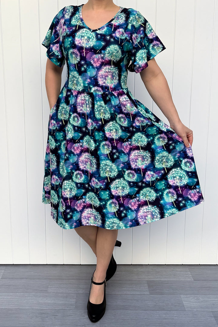 Woman wearing a colorful dress with a dandelion pattern against a white wooden panel background