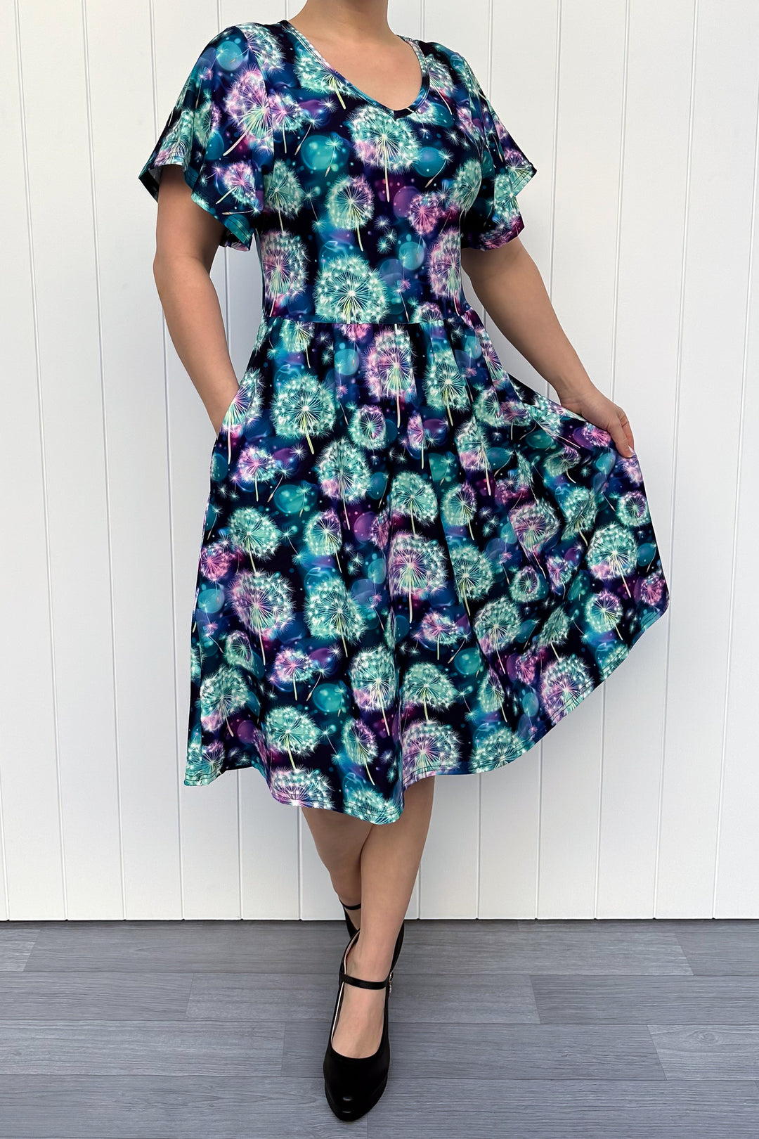 Woman wearing a colorful dandelion pattern dress against a white wooden panel background