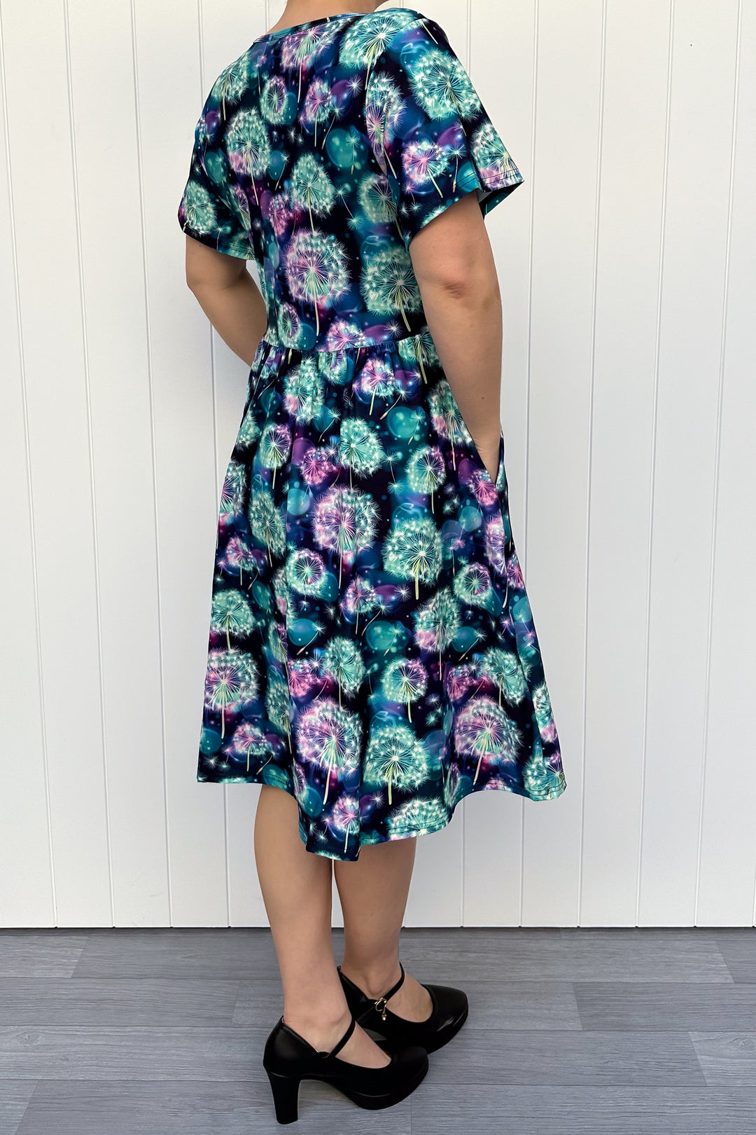 Person wearing a floral dress against a white wooden panel background