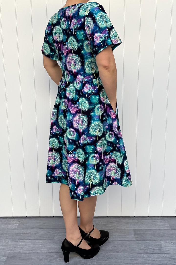 Person wearing a floral dress against a white wooden panel background