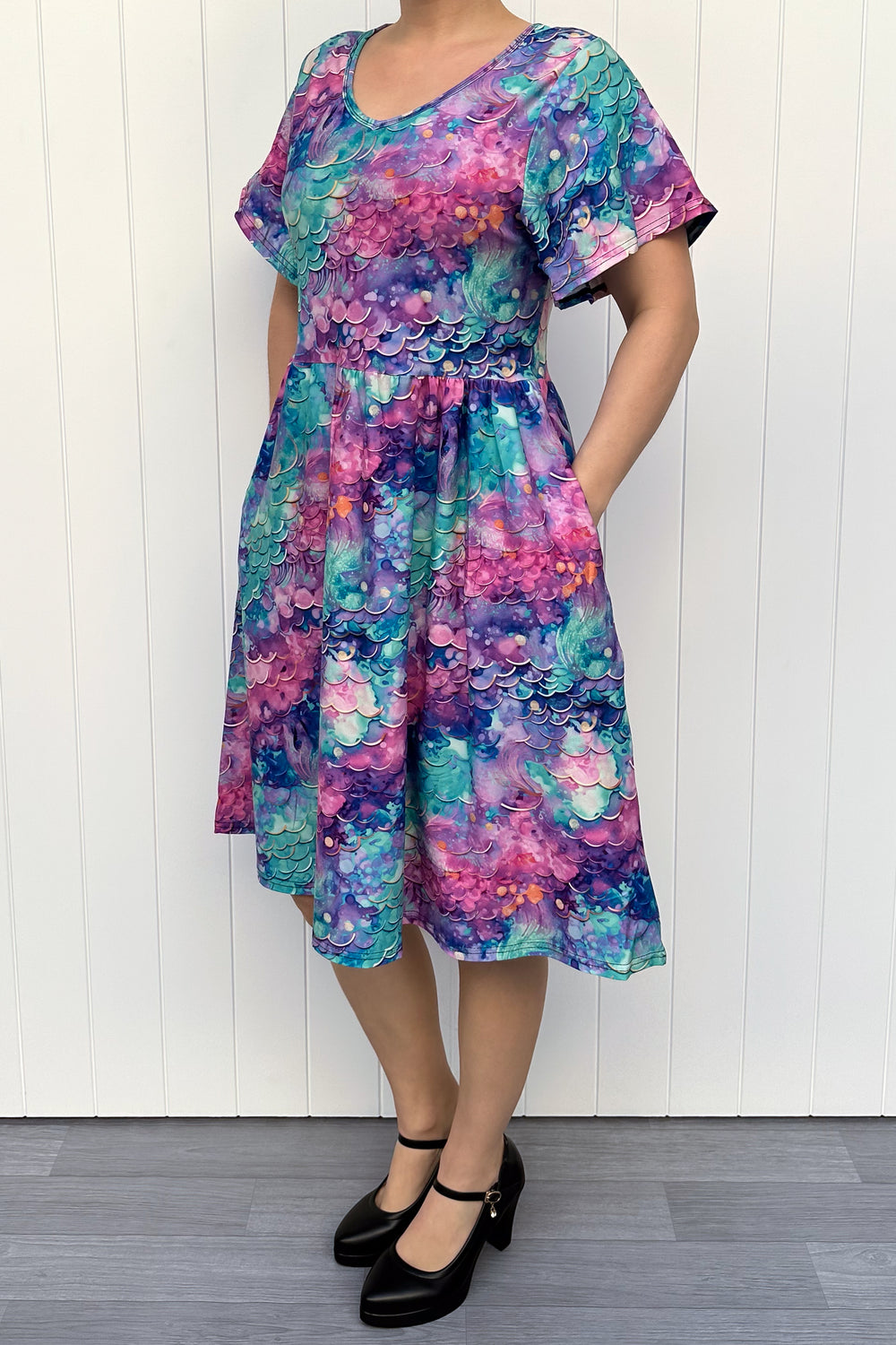 Person wearing a colourful mermaid siren pattern dress against a white wooden panel background