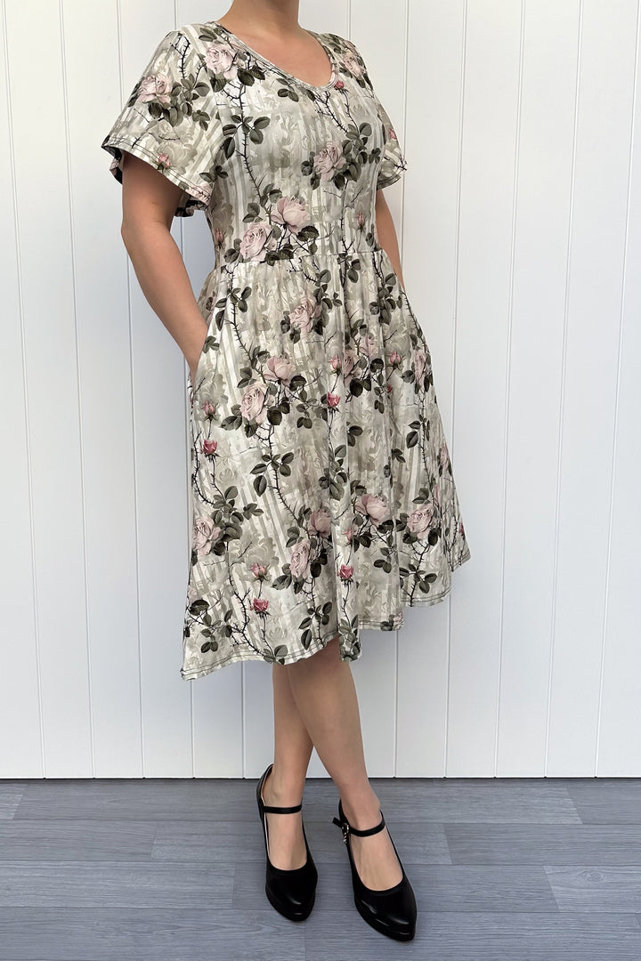 Woman wearing a floral dress standing against a white wooden panel background