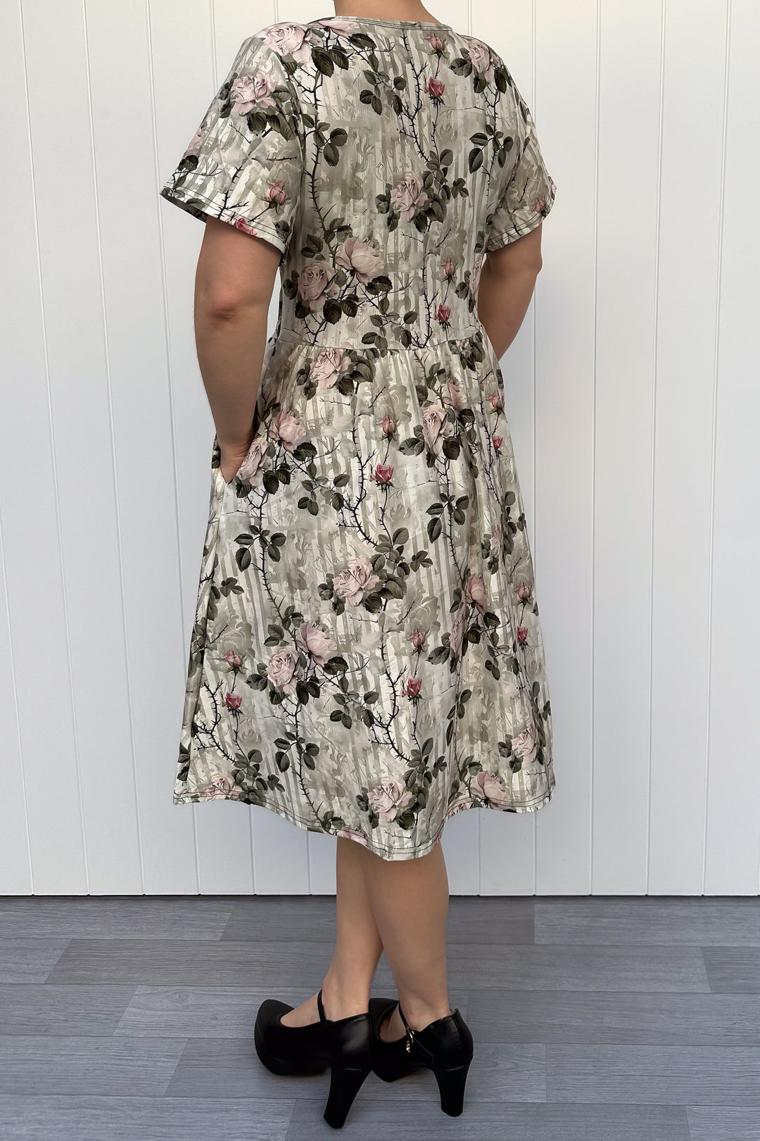 Person wearing a floral dress against a white wooden panel background