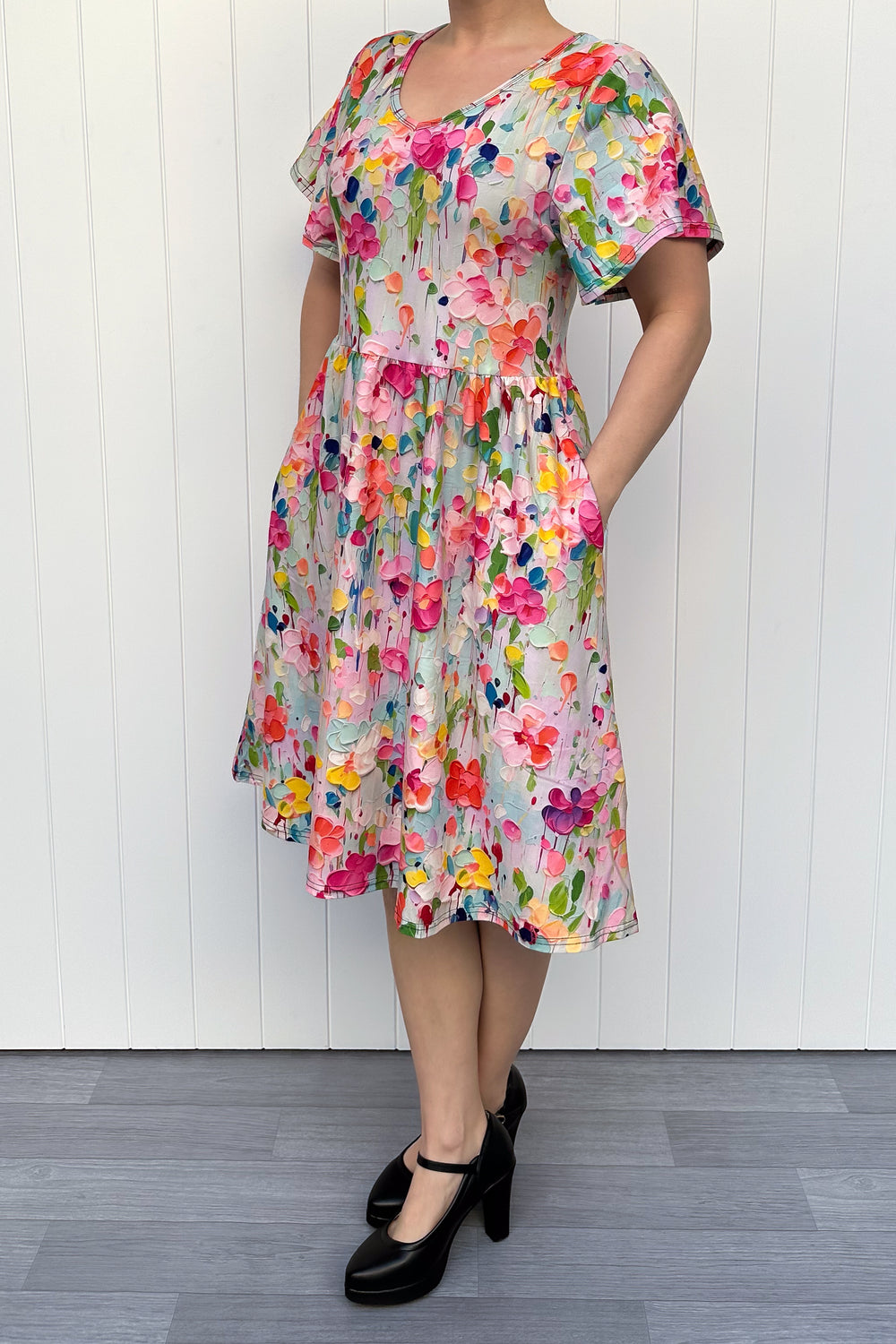Woman wearing a colorful floral dress against a white wooden panel background