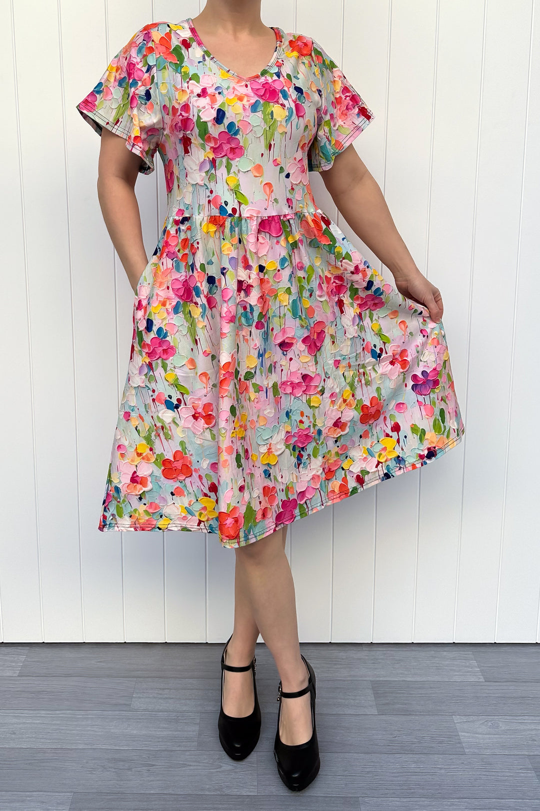 Person wearing a colorful floral dress against a white wooden panel background