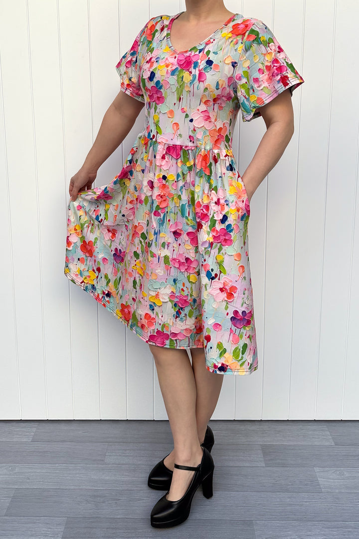 Woman wearing a colorful floral dress against a white wooden panel background