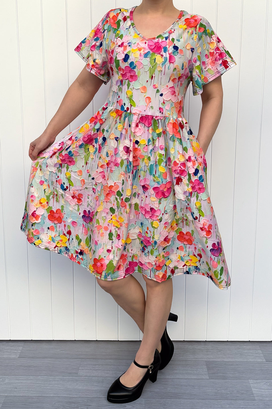 Woman wearing a colorful floral dress against a white wooden panel background