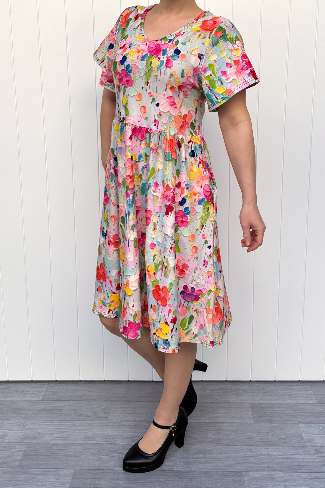 Woman wearing a colorful floral dress against a white wooden panel background
