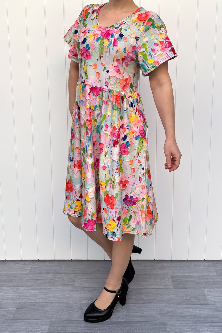 Woman wearing a colorful floral dress against a white wooden panel background