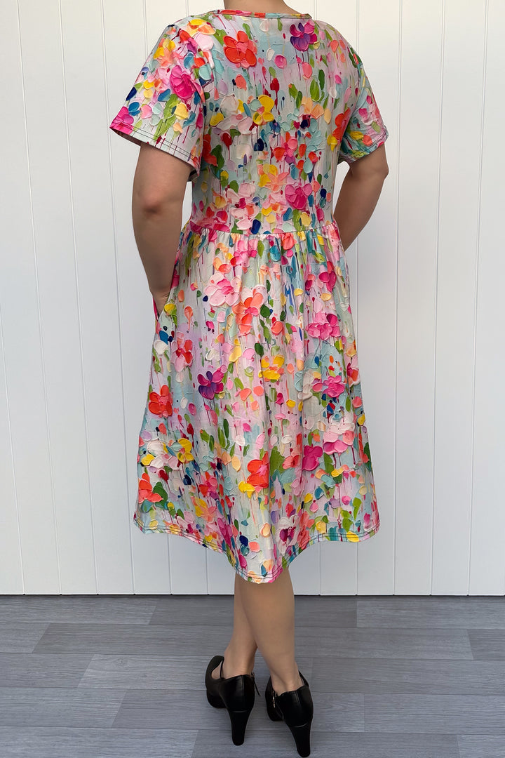 Person wearing a colorful floral dress against a white wooden panel background