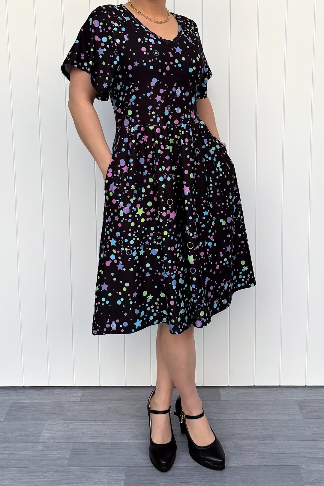 Person wearing a black dress with colorful star pattern against a white wooden panel background