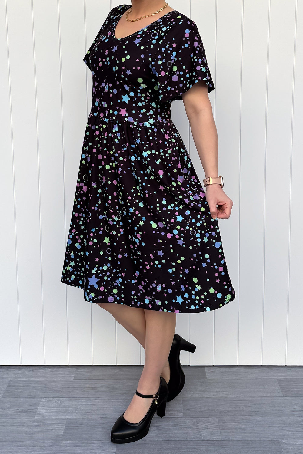 Woman wearing a black dress with colorful patterns against a white wooden panel background