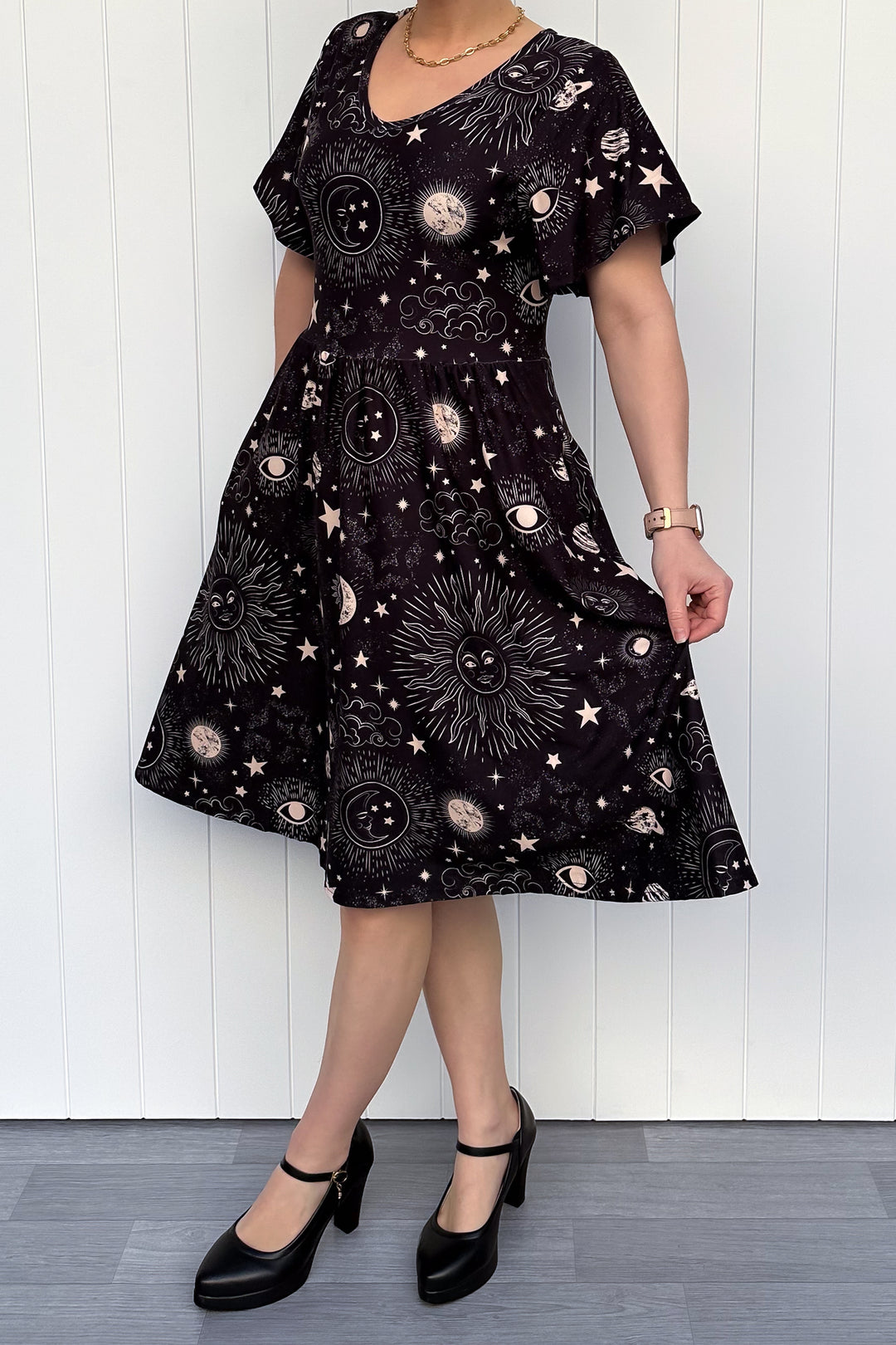 Person wearing a black dress with celestial pattern against a white wooden panel background