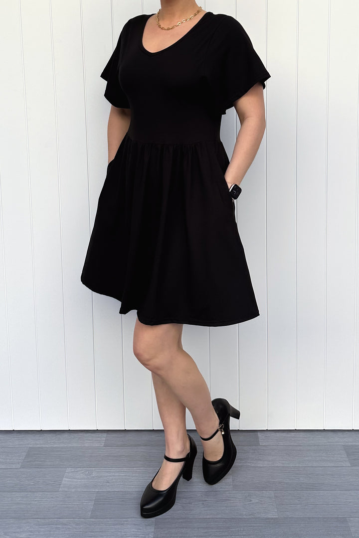 Person wearing a black dress standing against a white wooden panel background