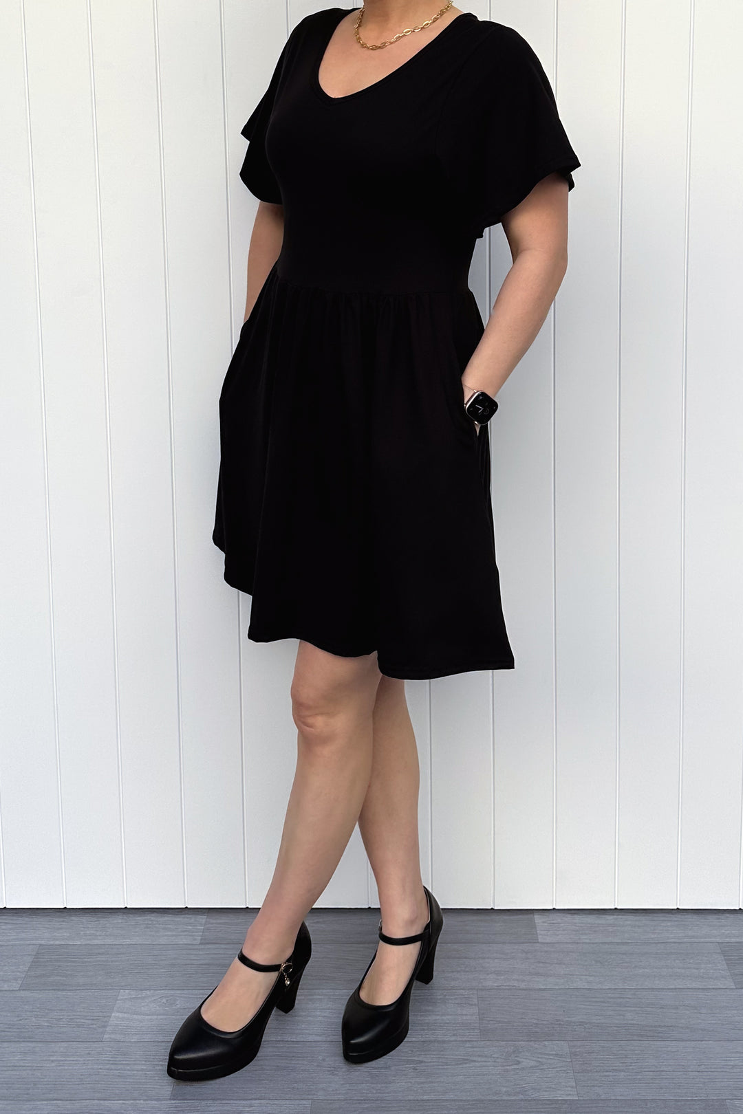Person wearing a black dress standing against a white paneled wall.