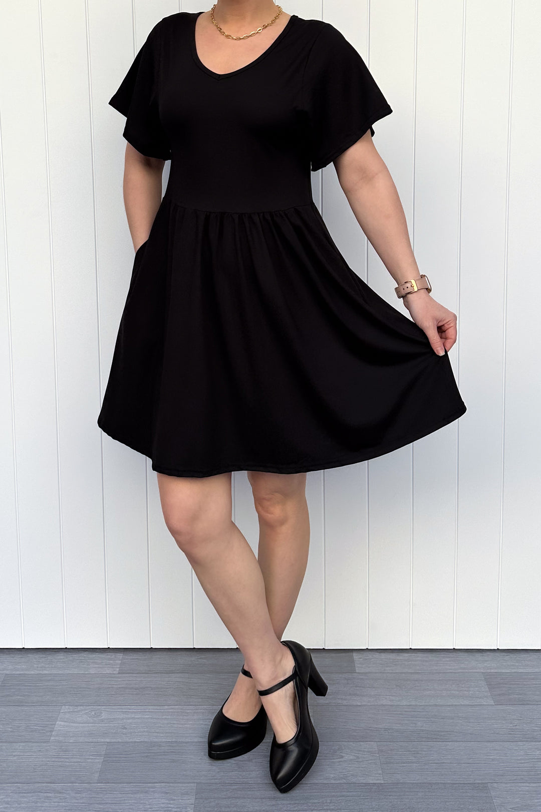 Person wearing a black dress against a white wooden panel background