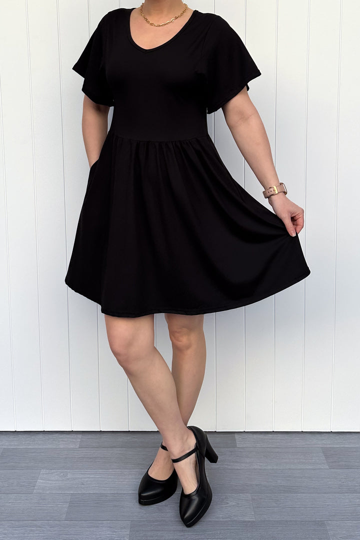 Person wearing a black dress against a white wooden panel background