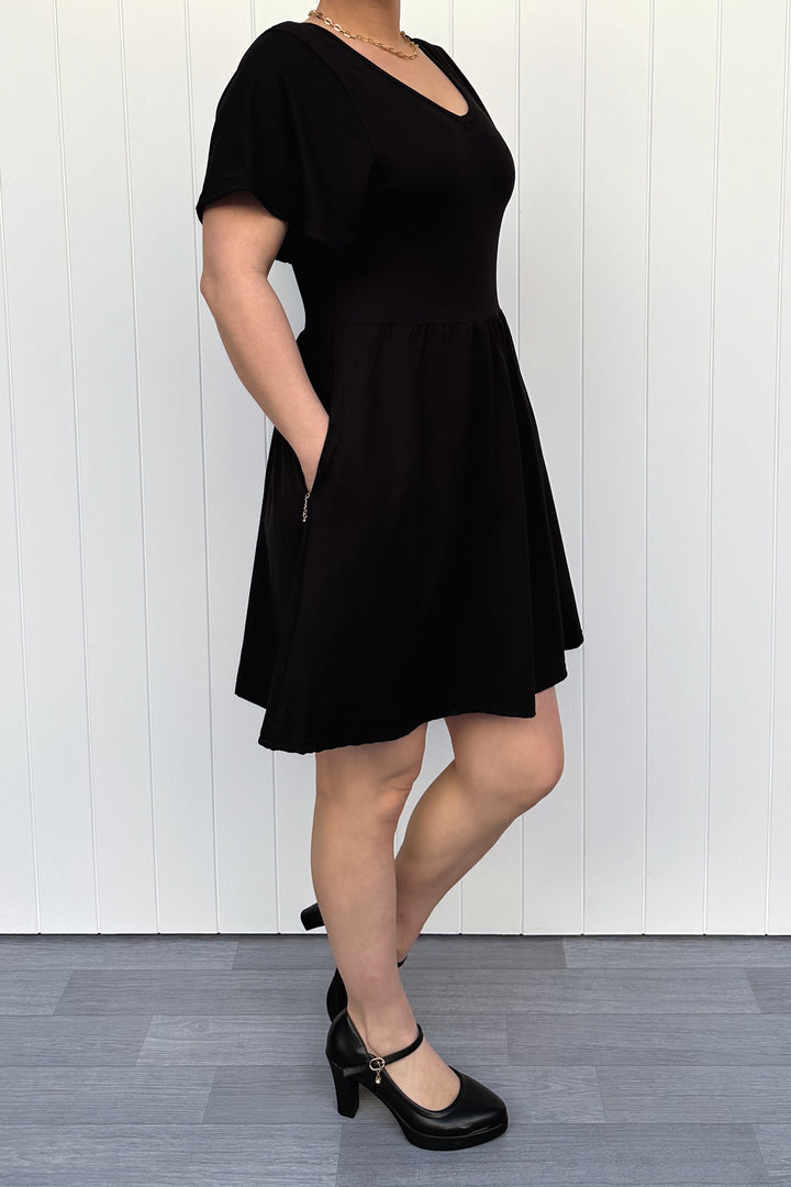 Person wearing a black dress standing against a white wall.